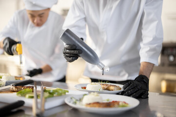 Multiracial group of cooks finishing main courses while working together in the kitchen. Team prepares meals for the restaurant 