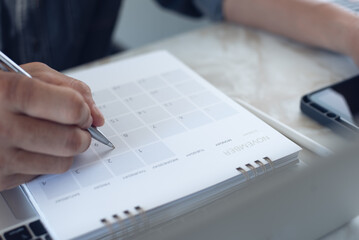 Close-up of  businessman making agenda on personal organizer on desktop calendar and planner at workplace, event planning concept