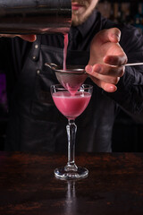 Bartender dressed in black apron and shirt make pink cocktail drink on black background