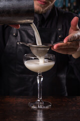 Bartender dressed in black apron and shirt make whie cocktail drink on black background