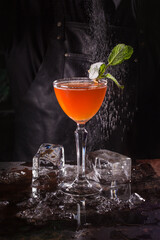 Bartender dressed in black apron and shirt make orange cocktail drink on black background