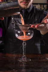 Bartender dressed in black apron and shirt make red cocktail drink on black background