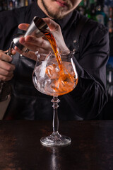 Bartender dressed in black apron and shirt make red cocktail drink on black background