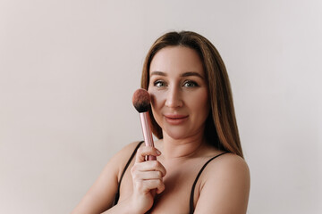 A beautiful young woman makeup artist with clean facial skin makes herself a natural fresh makeup using a cosmetic brush and powder on a white isolated background. Selective focus