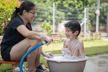 Asian boy showers in a bucket with his mother.
