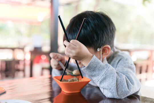 Asian boy eating noodle with chopsticks and a face mask