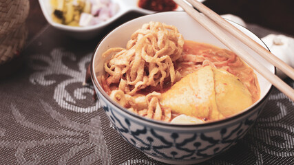 Thai Food, Northern Style Curried Noodle Soup or what we call in thai "Khao Soi" served in a Thai style patterned bowl. on brown wooden table