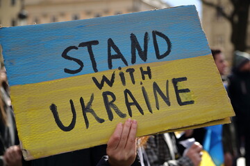 Banner in national colour of Ukraine and slogan STAND WITH UKRAINE in protester hand during street demonstration against Russian aggression