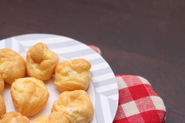 The eclair is placed in a white plate on a wooden table.