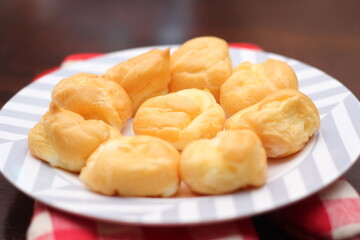 The eclair is placed in a white plate on a wooden table.