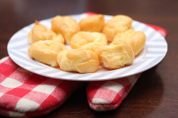 The eclair is placed in a white plate on a wooden table.