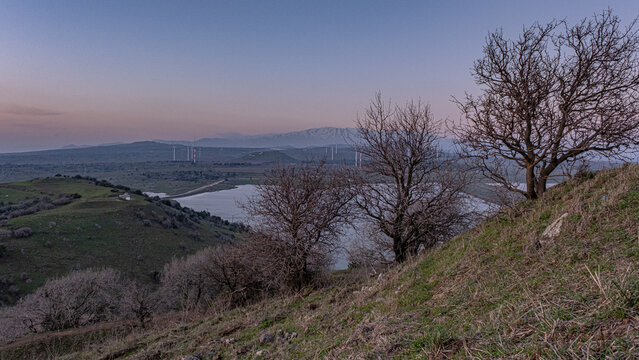 Top view of Bental water reservoir, the Golan hills with wind turbines and the Hermon Mountain Range at sunset as seen from Mount Bental summit, Golan Heights, Israel.
