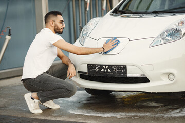 Indian man wiping his white transportation on car wash after washing