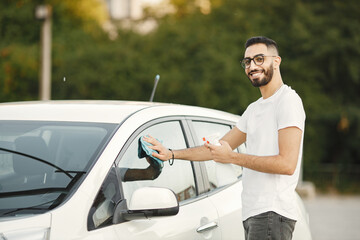 Indian man wiping his white transportation on car wash after washing