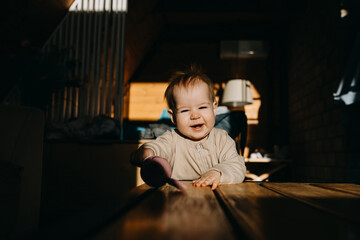 little child laughing, playing with a toy at home in sun light, looking at camera.
