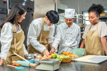 Students In Cookery Class Mixing Ingredients For Recipe In Kitchen.Male And Female young  Students With chef Teacher Preparing Ingredients For Dish In Kitchen Cookery Class.
