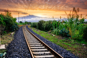 Obraz na płótnie Canvas old evening railroad leading to a sunset glow in mountains with green bushes and cjlorful cloudy sku on the background