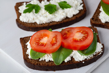 Slice of rye bread with cottage cheese and tomatoes on a wooden cutting board