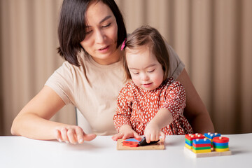 cute baby girl with down syndrome learning with educational toys at home with mom,child special education in the family