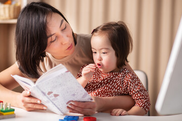 training and education of children with down syndrome, a girl with her mother and a book at home read a textbook © yta