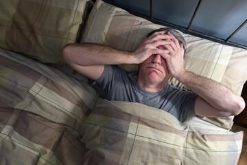 Fototapeta premium Man with insomnia lying in bed and snorting from exhaustion.