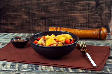 Boiled potatoes with meat in a black bowl. Potatoes with mushrooms and carrots. Boiled mushrooms and chicken with potatoes. Food on a black wooden table.