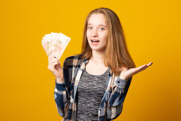 Happy young woman holding Russian rubles, received a scholarship, a salary on a yellow background....