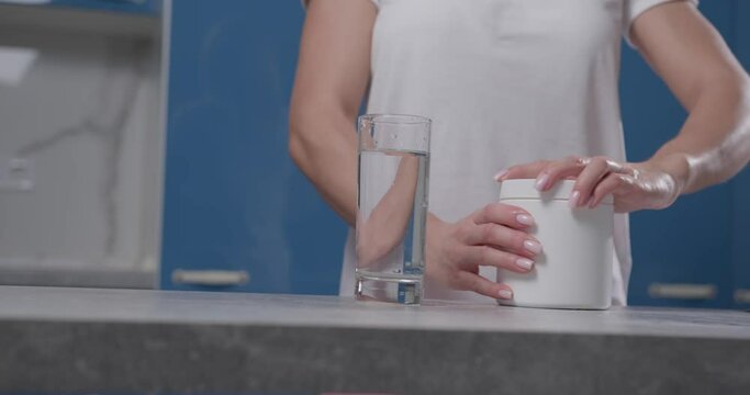A woman's hand opens a white jar, pours bcaa into a glass and stirs it.