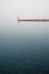 Minimalist landscape with still water and wooden jetty in the morning foggy river. Dreamy tranquil...