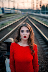 Fototapeta premium portrait beautiful young woman in a long red dress stands near the railway