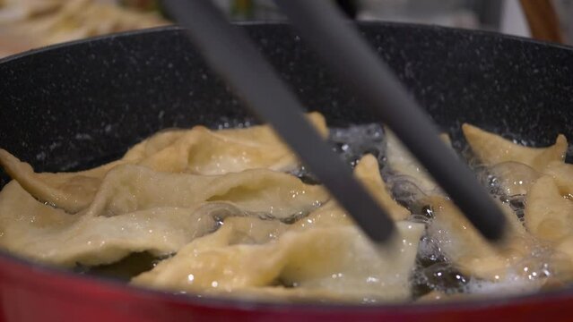 Cooking Angel Wings In Deep Frying Pan With Oil, Flipping With Tongs. close up
