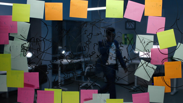 View through glass board with notes of businessman talking on smartphone in office - Powered by Adobe