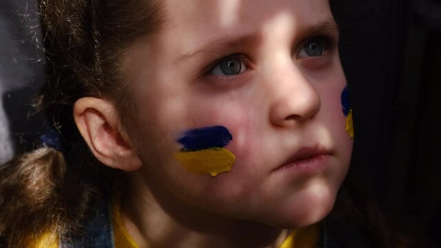 Portrait of upset little child girl with flags of ukraine on face. Peace, no war, help, stop russian aggression. Freedom to Ukraine, Crisis concept. Hope for the world. Anxiety and anticipation