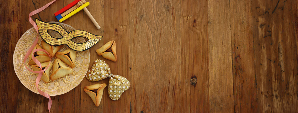 Purim celebration concept (jewish carnival holiday). Hamantaschen cookies and gold carnival mask over wooden background