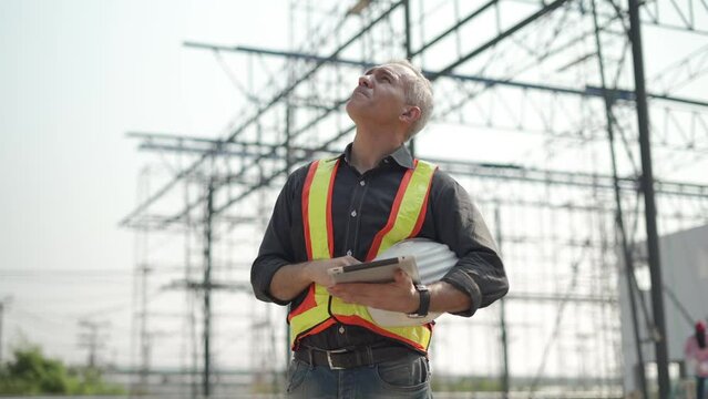 senior construction worker or architect using digital tablet checking structure in construction site outdoors with Hot weather sunny . builders taking off hard hat inspecting and working in workplace