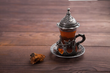 Chaga mushroom tea in a Turkish cup and a piece of chaga on a wooden background. Copy spaes