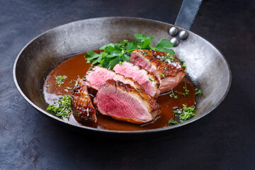 Traditionell gegrilltes Gourmet Entenbrust Filet mit Haut serviert mit Dunkelbier Sauce als close-up in einer rustikalen Bratpfanne