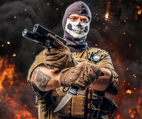 Special force soldier with pistol and knife against burning background