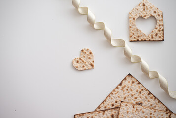 Layout of Traditional Matzah prepared for Passover with Matzah shape of heart, ribbon and house with heart  on white table. top view. Spring Holiday of Jewish people. Fasting time. Spase for text