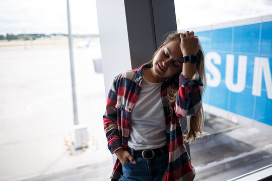 A beautiful attractive ukrainian woman with blond hair is standing by a large window, wearing momom jeans and a t-shirt with a plaid shirt. Girl in casual comfortable clothes
