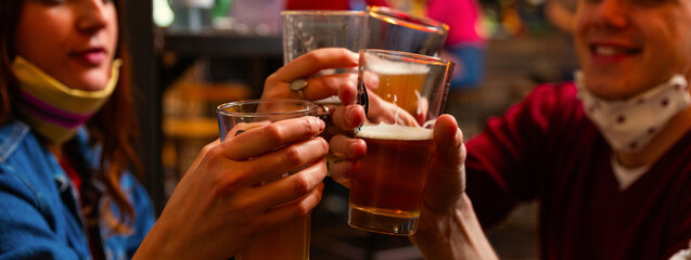 Happy young people drink and toast with beer in a pub. - Detail of hands while toasting with glasses of beer - group friend drink at a bar party – happy hour in a pub -  horizontal banner or header