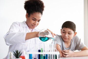 Smiling African black woman is studing and testing for chemical and science. She is experimenting and teaching Caucasian studen boy at laboratory Lab of school. Education and knowledge concept.