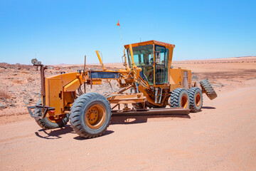 Yellow grader smooths dirt road in namib deserts - Road grader smoothing a dirt road in a rural...