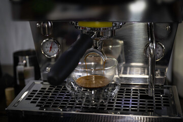 In coffee shop,coffee maker mechine pouring hot fresh coffee into a cup of clear glass cup.