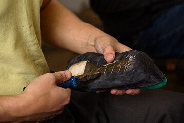 Shoemaker making shoes sitting in workshop. Bootmaker removing nails with pliers from gray suede boot on shoe last. Closeup.