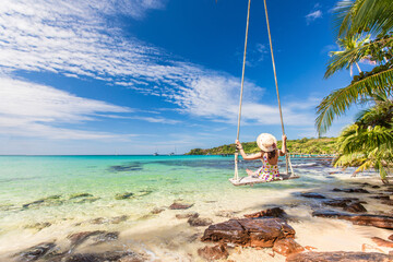 Young woman sitting on swing with beautiful tropical sea.