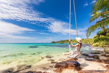 Young woman sitting on swing with beautiful tropical sea.