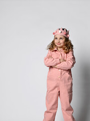 cute girl with a plush crown, stands in full growth with her arms folded on her chest, in a closed pose. in a cotton summer jumpsuit, dusty rose color, with comfortable pockets. on a light background.