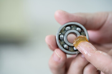 Worker use finger to put lithium grease into small bearing at laboratory. Yellow transparance grease on the finger. Testing and service concept. Preventive maintenance and checking bearing damage .