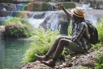 African Man Traveller with backpack sitting for selfie and relaxing freedom at the waterfall.